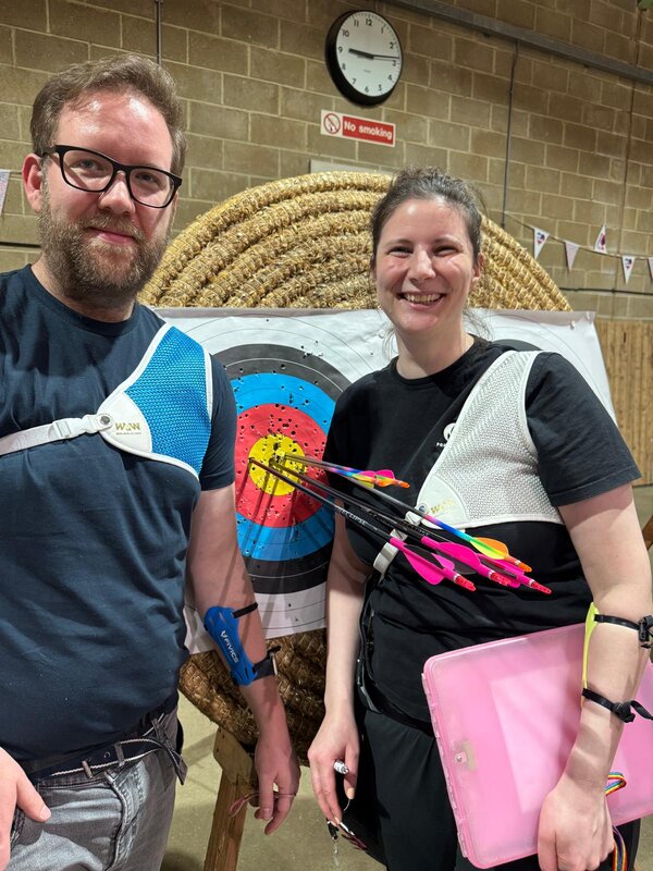 Chris and Ruth smiling in front of a target at an indoor shoot